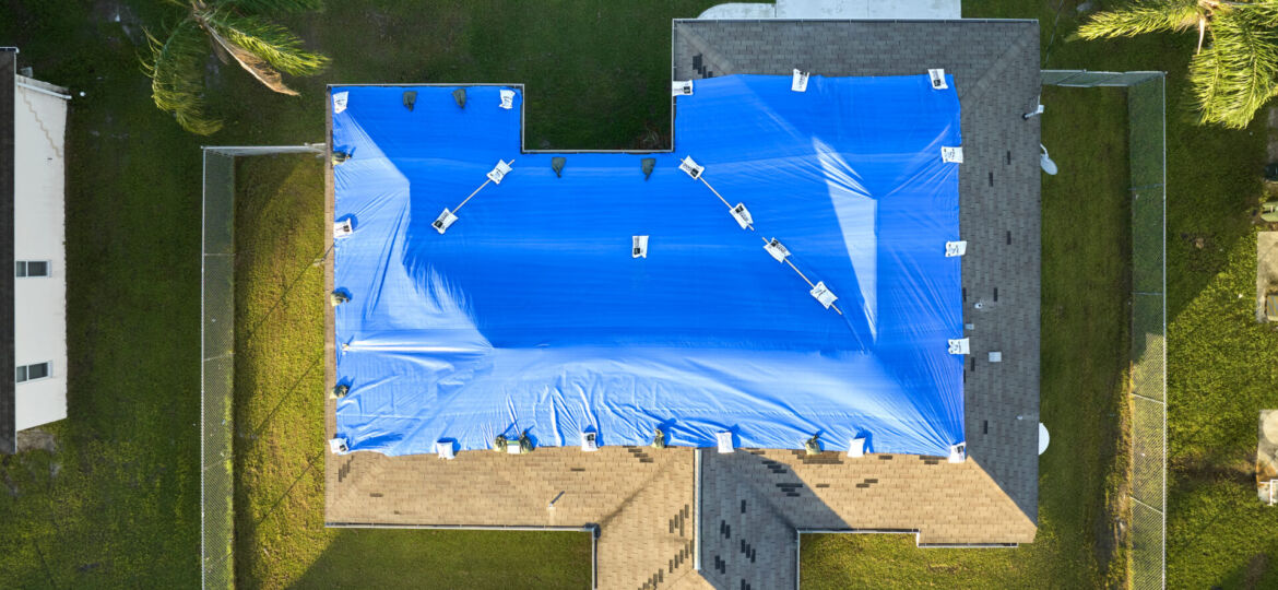 Hurricane Ian damaged house rooftop covered with protective plastic tarp against rain water leaking until replacement of asphalt shingles. Aftermath of natural disaster