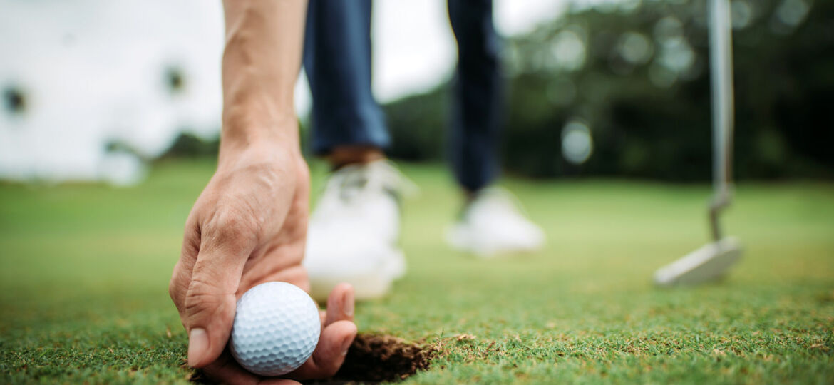 Close up of asian chinese young male golfer picking up golf ball with hand at the hole of golf course