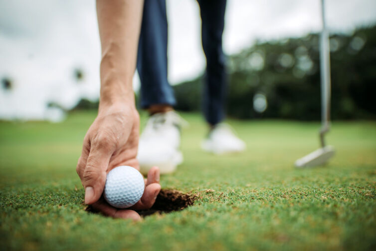 Close up of asian chinese young male golfer picking up golf ball with hand at the hole of golf course